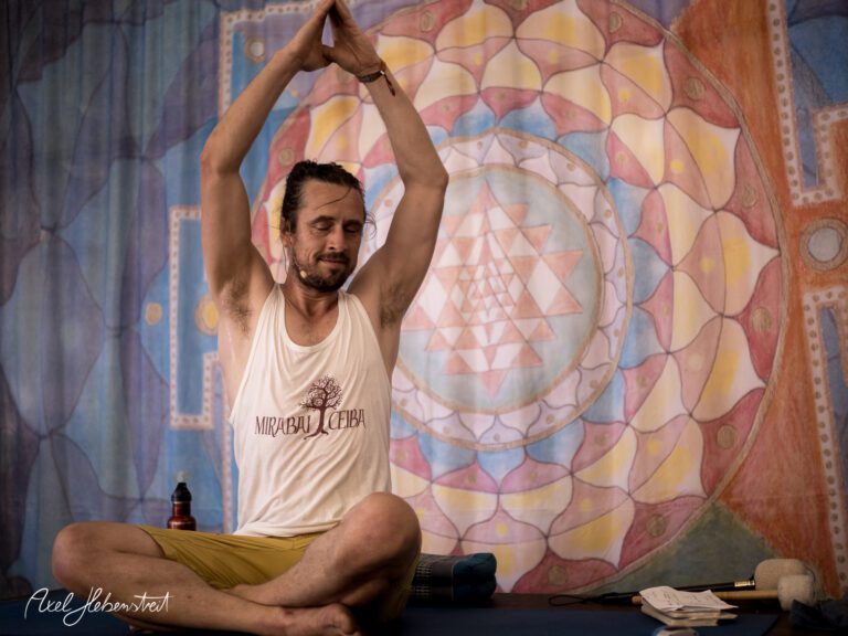 Mann in Yogapose mit erhobenen Händen, entspannt vor buntem Mandala-Hintergrund – © Axel Hebenstreit