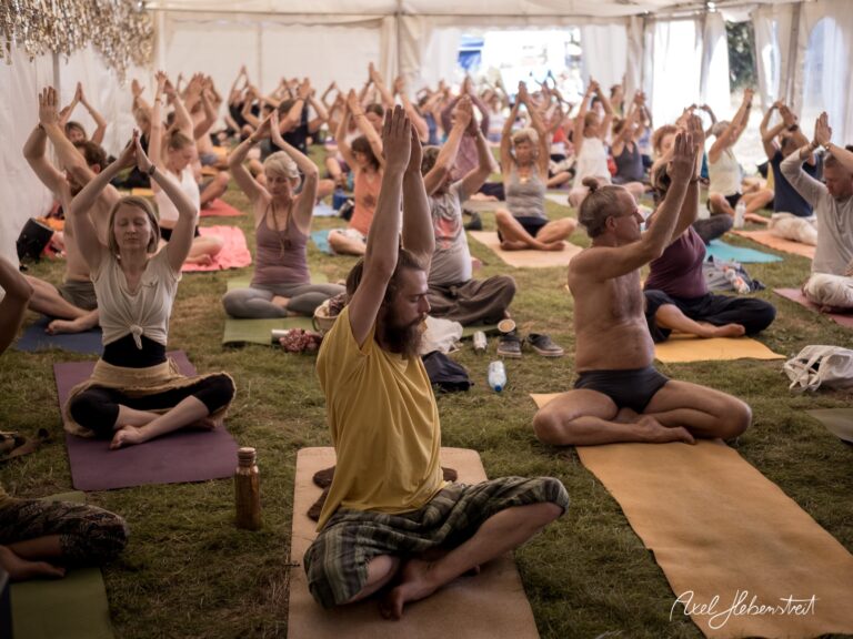 Eine große Gruppe von Menschen praktiziert Yoga in einem Zelt bei einem Festival, harmonische Stimmung und Konzentration – © Axel Hebenstreit