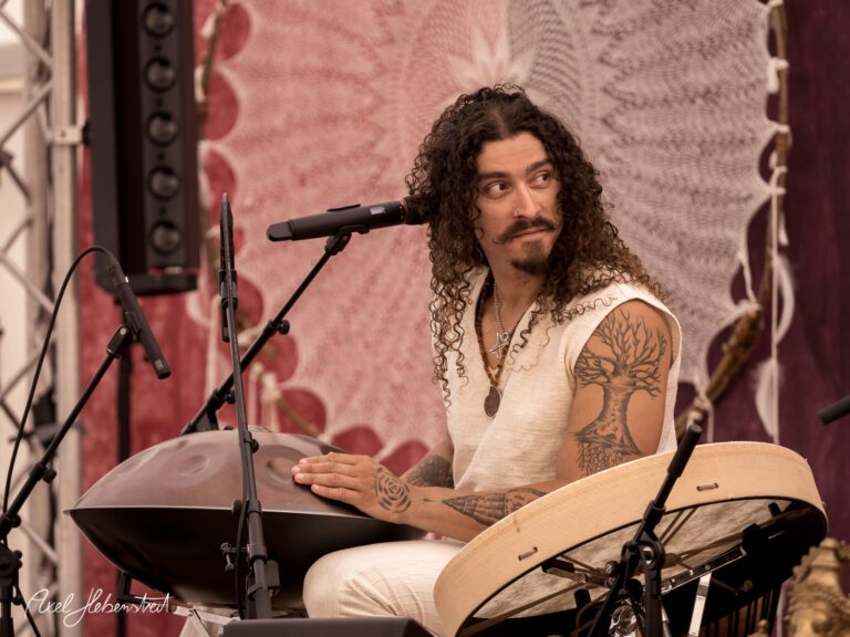 Musiker mit lockigem Haar spielt leidenschaftlich auf einem Handpan während eines Festivals – © Axel Hebenstreit