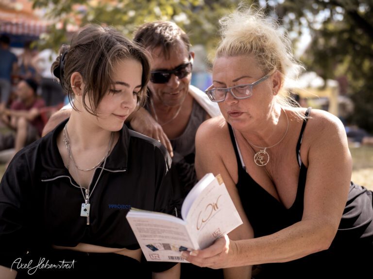 Junge und Erwachsene schauen interessiert in ein Buch, während sie in einem entspannten Park sitzen – © Axel Hebenstreit