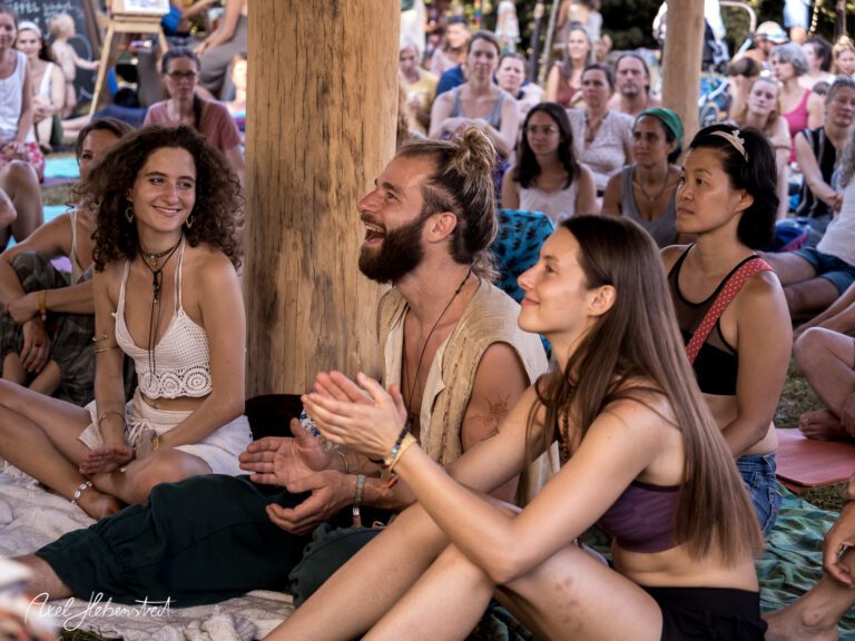 Lächelnde Menschen sitzen im Kreis, applaudieren begeistert bei einer Veranstaltung im Freien – © Axel Hebenstreit