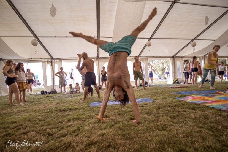 Ein Mann zeigt einen Handstand in einem Zelt während eines Festivals, umgeben von begeisterten Zuschauern. – © Axel Hebenstreit