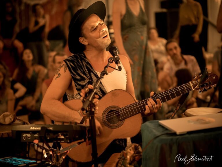 Musiker mit Gitarre in einem stimmungsvollen Konzert, umgeben von einem begeisterten Publikum – © Axel Hebenstreit