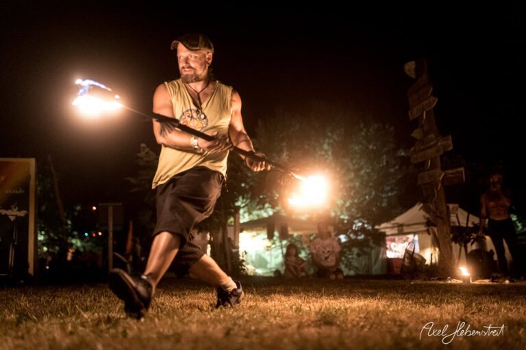Ein Feuerkünstler führt mit Fackeln einen beeindruckenden Tanz in der nächtlichen Festivalatmosphäre auf. – © Axel Hebenstreit