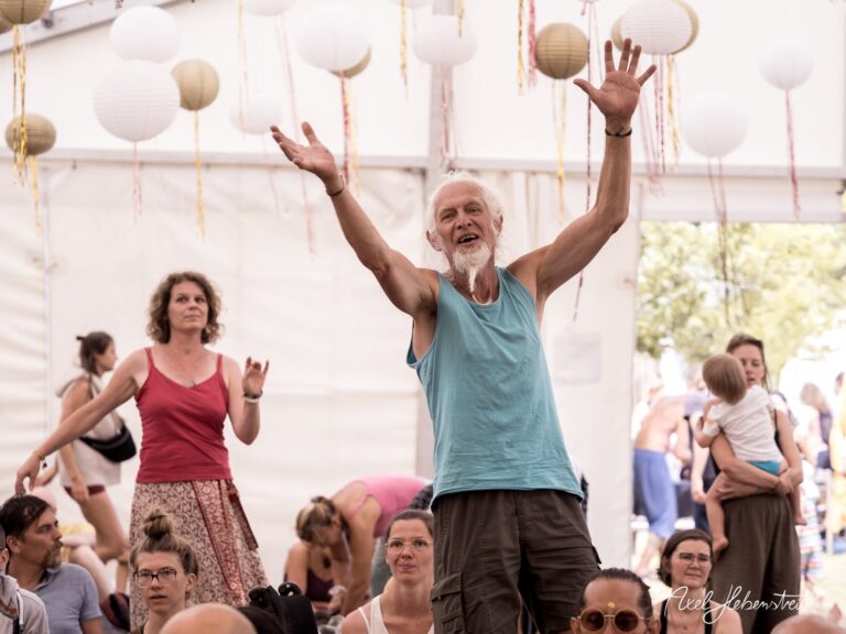 Ein enthusiastischer Mann mit weißen Haaren und Bart hebt die Arme voller Freude in einem Festzelt. – © Axel Hebenstreit