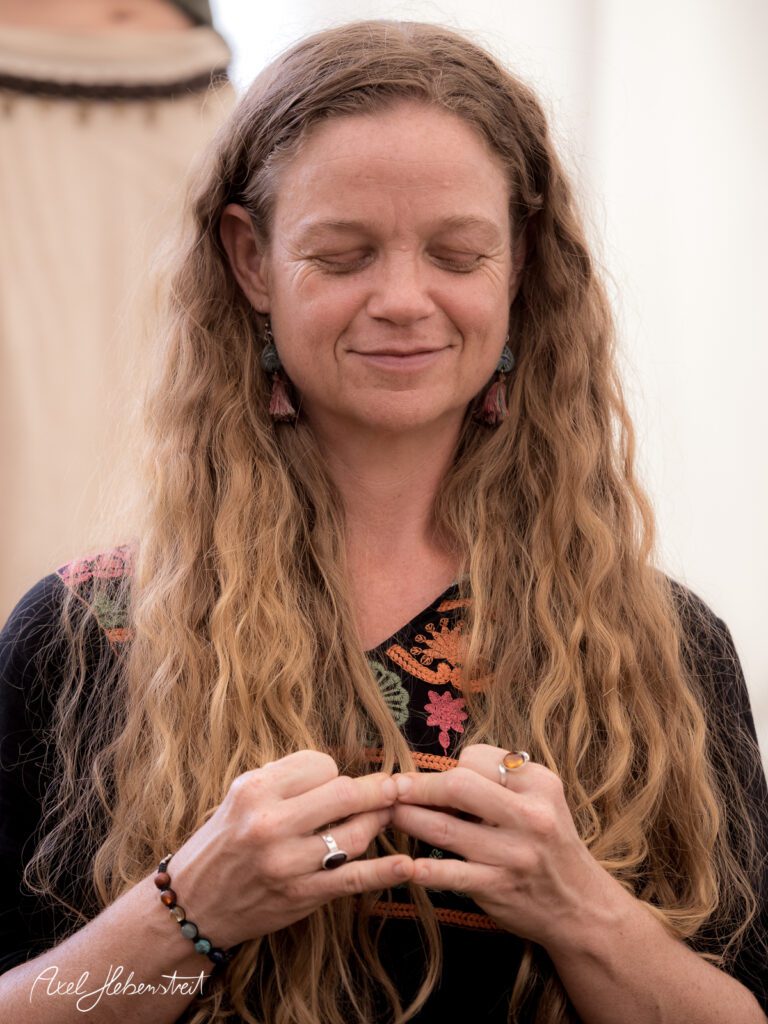 Eine Frau mit langen Locken meditiert und hält ihre Hände in einer entspannten Position – © Axel Hebenstreit