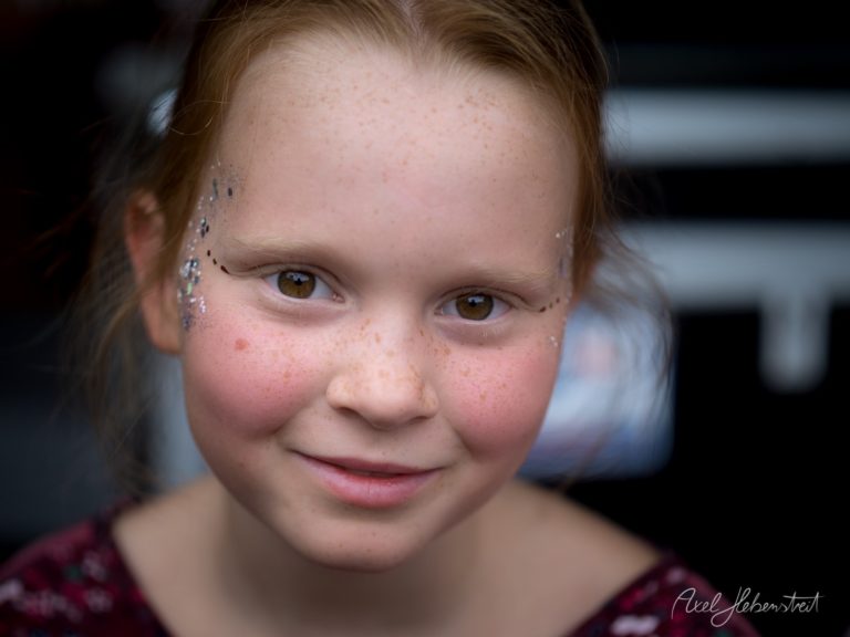 Lächelndes Mädchen mit Glitzer-Gesichtsbemalung in festlicher Atmosphäre – © Axel Hebenstreit