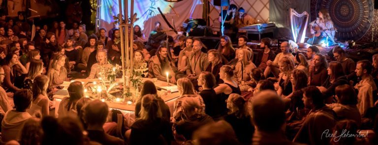 Farbenfrohe Festivalatmosphäre mit Menschen, die um einen mit Kerzen beleuchteten Tisch versammelt sind – © Axel Hebenstreit