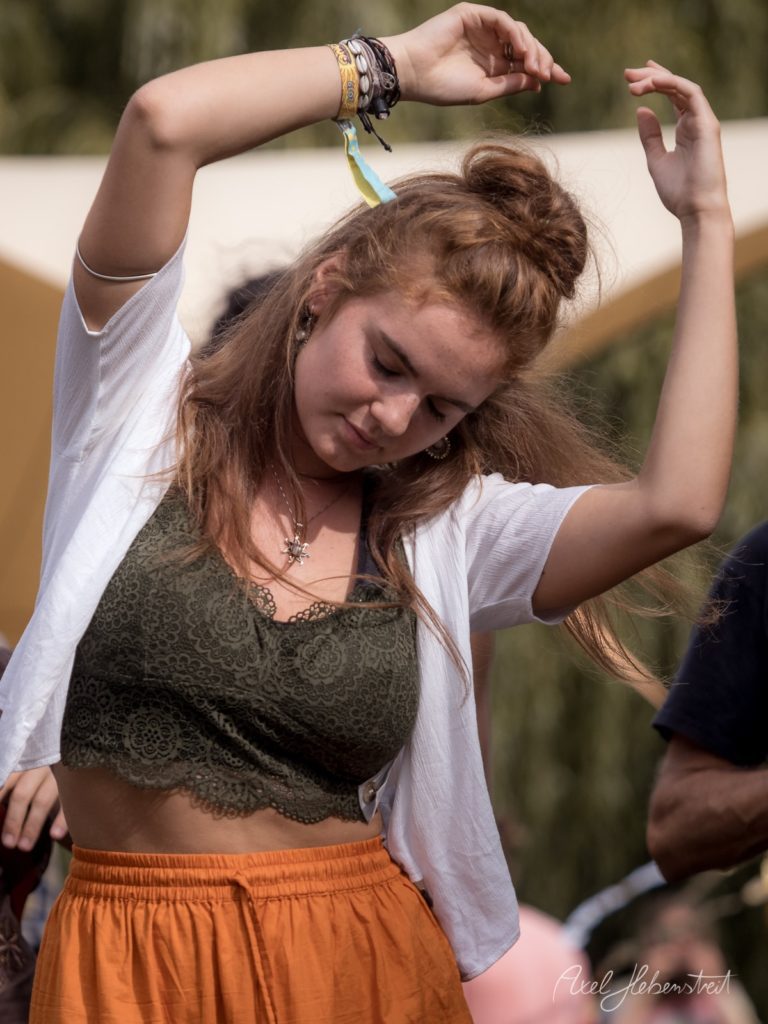 Junge Frau tanzt fröhlich auf einem Festival, trägt ein top und einen weiten Rock, umgeben von entspannter Atmosphäre – © Axel Hebenstreit.