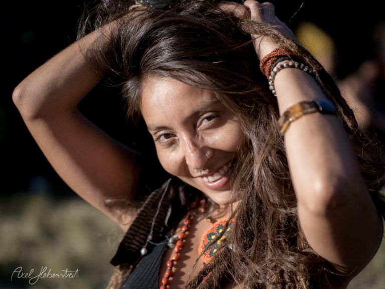 Lächelnde Frau mit langen Haaren und bunten Accessoires, die fröhlich im Freien ihre Haare spielt – © Axel Hebenstreit
