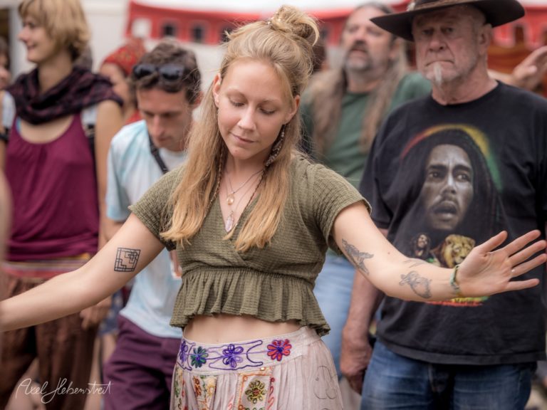 Eine tanzende junge Frau mit Tattoos in lässiger Kleidung, umgeben von festivalbegeisterten Menschen – © Axel Hebenstreit