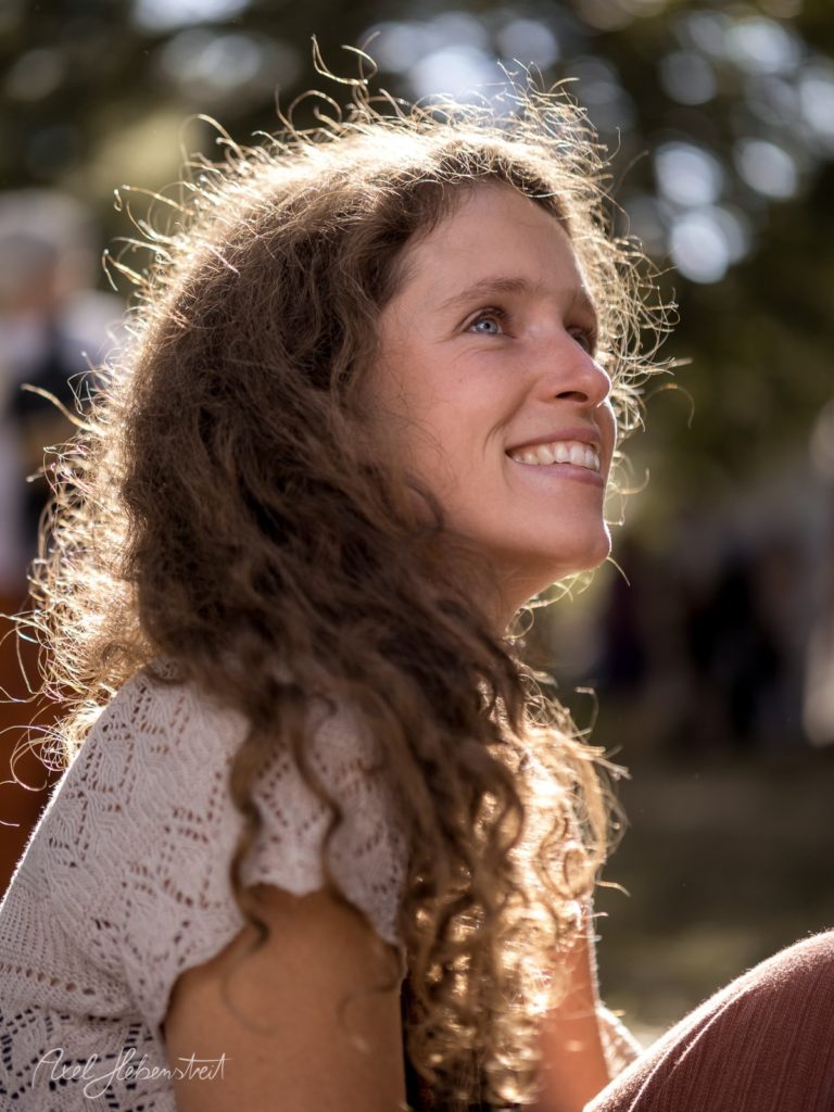 Fröhliche Frau mit lockigem Haar, die gebannt in den Himmel schaut, umgeben von natürlichem Licht – © Axel Hebenstreit