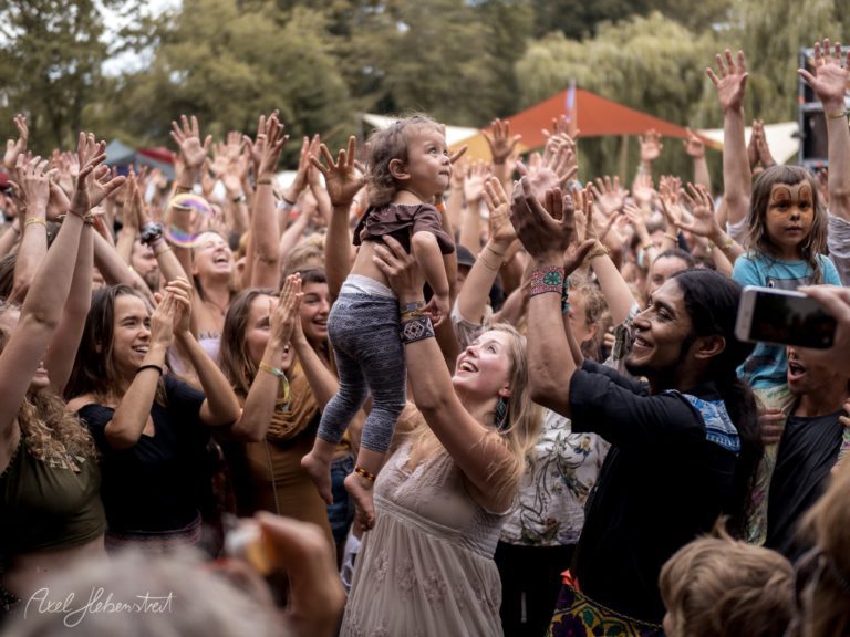 Eine jubelnde Menge feiert mit einem kleinen Kind in den Armen, umgeben von einer zauberhaften Festivalatmosphäre – © Axel Hebenstreit