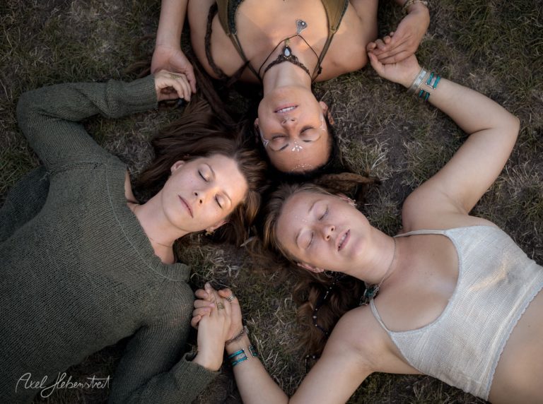 Drei Frauen liegen entspannt im Gras, halten sich an den Händen und genießen eine friedliche, meditative Atmosphäre – © Axel Hebenstreit.