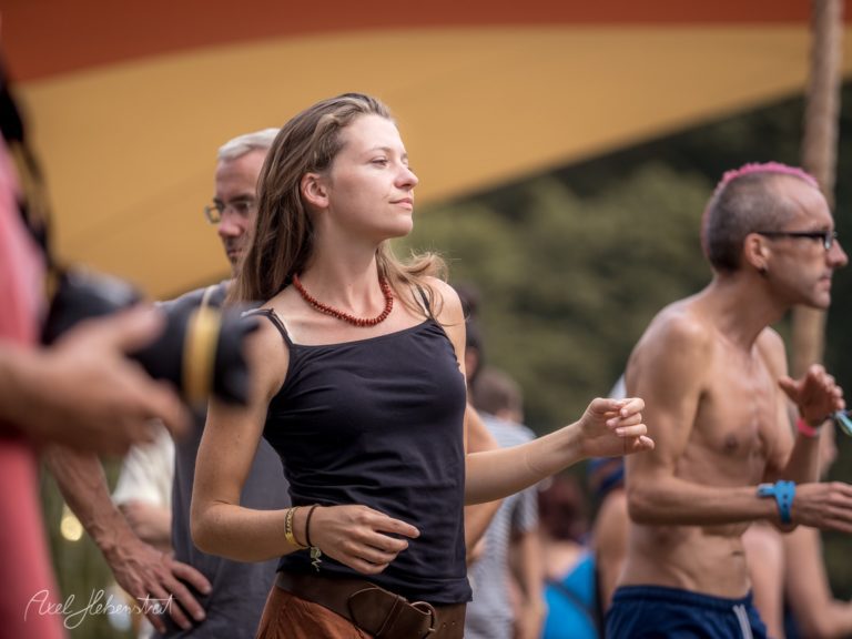 Eine Frau tanzt entspannt auf einem Festival im Freien, umgeben von weiteren Feiernden – © Axel Hebenstreit.