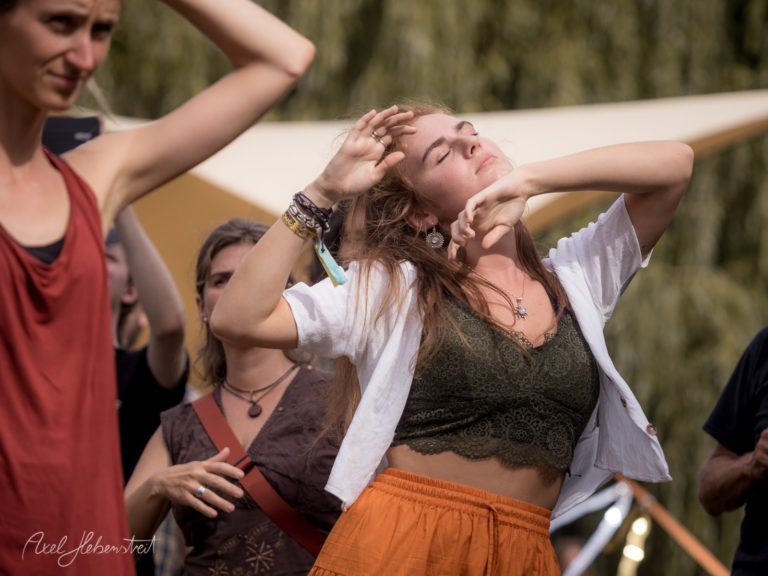 Frau tanzt ausgelassen auf einem Festival, umgeben von fröhlichen Menschen und sommerlicher Atmosphäre – © Axel Hebenstreit