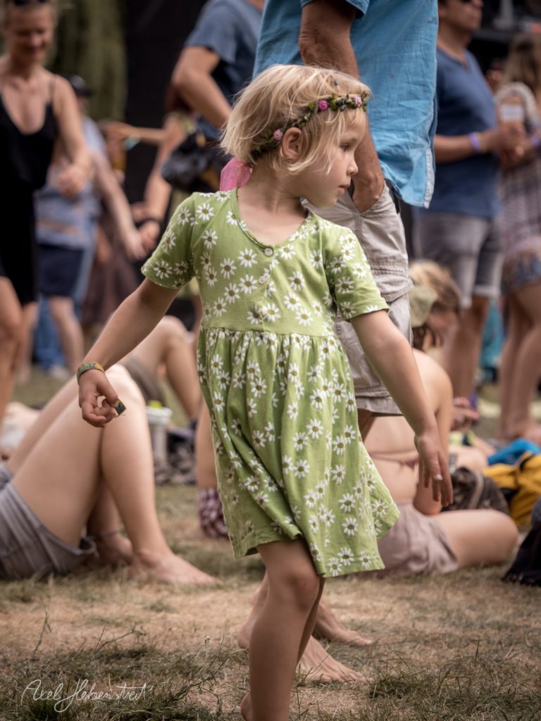 Ein kleines Mädchen im grünen Kleid tanzt fröhlich auf einem Festival im Freien. – © Axel Hebenstreit
