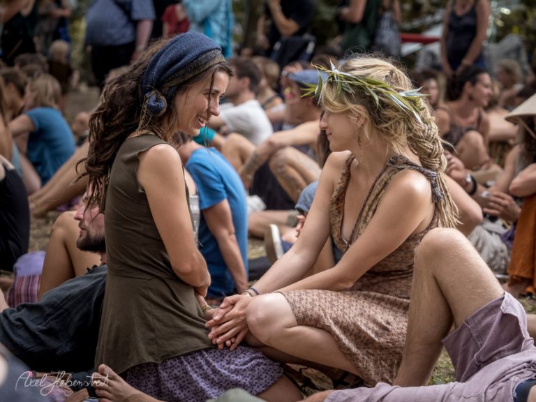 Zwei Frauen sitzen entspannt im Gespräch auf einer Wiese während eines Festivals – © Axel Hebenstreit.