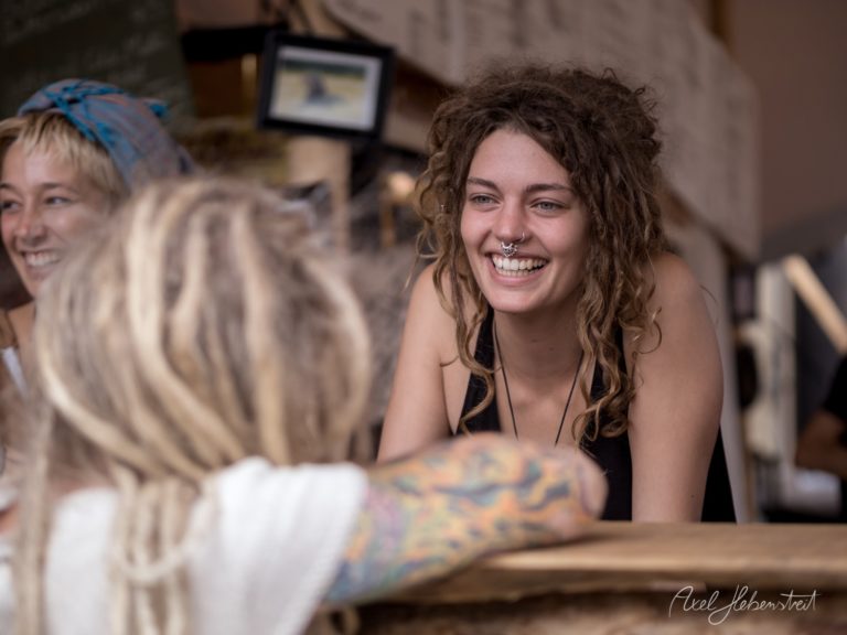 Lächelnde Frau mit Dreadlocks bedient freundlich einen Kunden in einem festlichen Ambiente – © Axel Hebenstreit