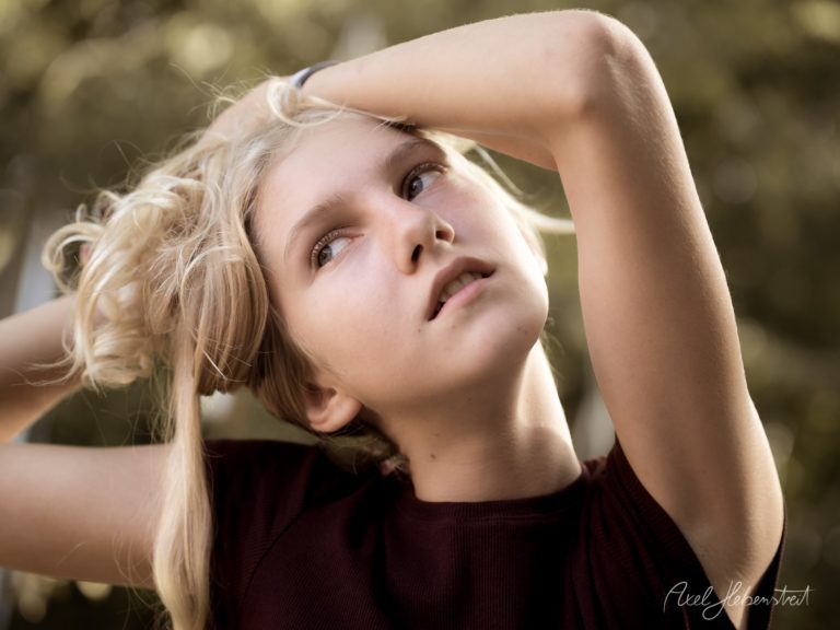 Junge mit blonden Haaren, die verwirrt den Kopf zur Seite neigt, umgeben von einer natürlichen Umgebung – © Axel Hebenstreit