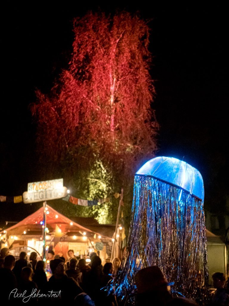 Bunter beleuchteter Quallen-Körper schwebt über einer Menschenmenge bei einem nächtlichen Festival – © Axel Hebenstreit