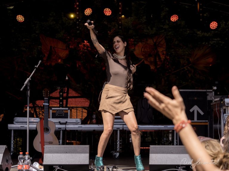 Dynamische Sängerin hebt das Mikrofon auf einer Festivalbühne und begeistert das Publikum – © Axel Hebenstreit