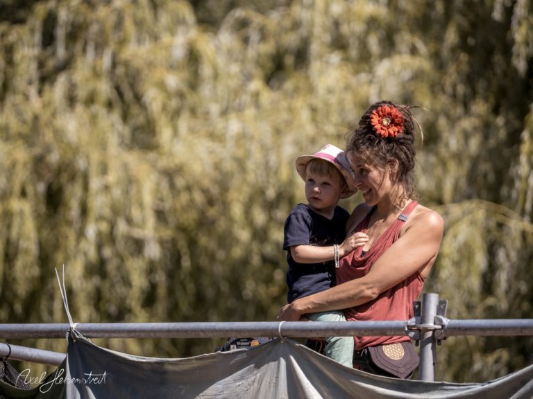 Eine Mutter hält ihr Kind in der Natur, umgeben von sanften Bäumen, und strahlt Freude und Zuneigung aus. – © Axel Hebenstreit