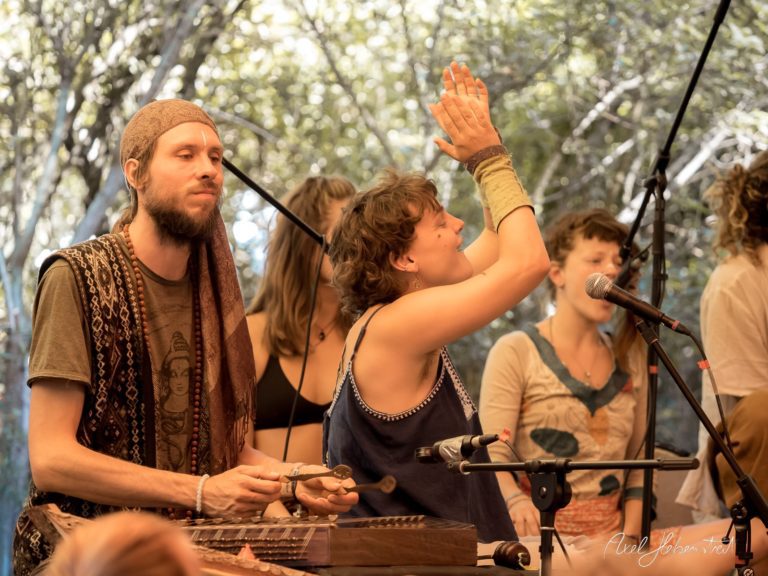 Musiker spielen mit Leidenschaft bei einem Festival, während eine Sängerin im Vordergrund begeistert mitsingt – © Axel Hebenstreit.