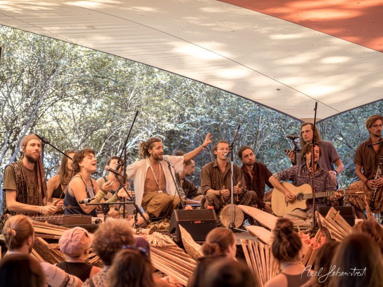 Musiker mit Instrumenten und singen im Freien während eines Festivals unter einem bunten Zelt – © Axel Hebenstreit