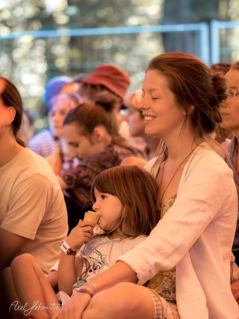 Eine Mutter sitzt entspannt mit ihrer Tochter im Arm während eines Festivals und genießt den Moment. – © Axel Hebenstreit