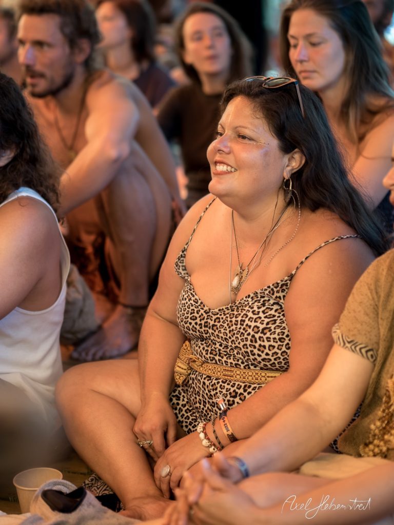 Lächelnde Frau im Leopardenmuster-Kleid, entspannt sitzend in einer Gruppe, umgeben von einer festlichen Atmosphäre – © Axel Hebenstreit