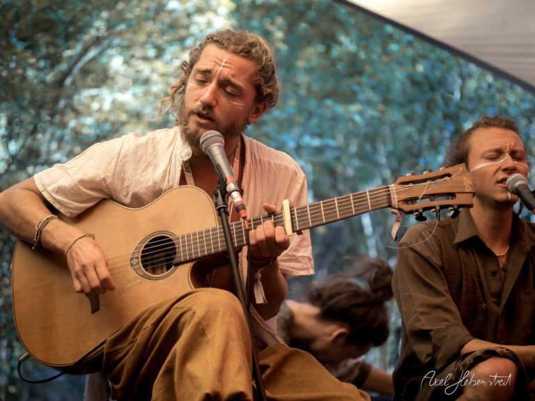 Musiker einer Live-Performance, der emotional Gitarre spielt und singt, umgeben von einer entspannten Festivalatmosphäre – © Axel Hebenstreit