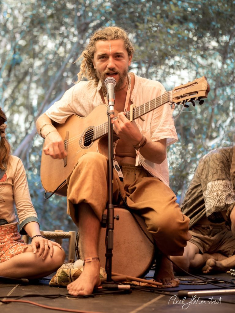 Musiker spielt mit Gitarre auf einer Bühne bei einem Festival, umgeben von einer entspannten Atmosphäre – © Axel Hebenstreit