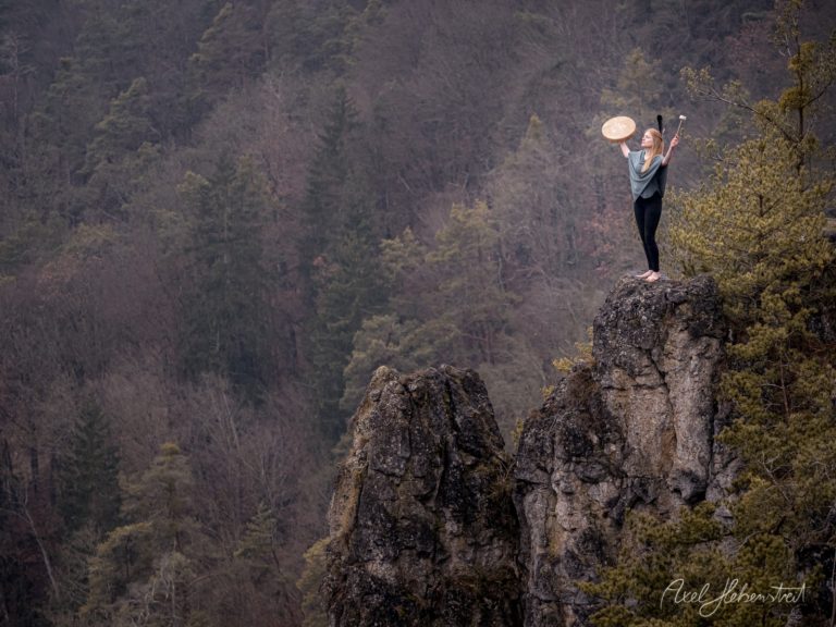 Frau steht auf Felsklippe mit Frisbee vor dichtem Wald in bergiger Naturlandschaft – © Axel Hebenstreit