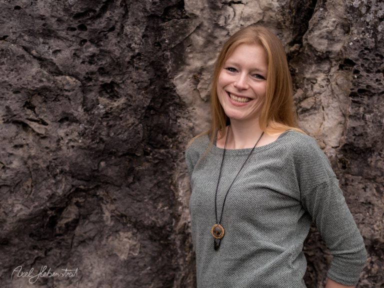 Porträt einer lächelnden Frau mit rötlichen Haaren vor einer rustikalen Steinwand – © Axel Hebenstreit