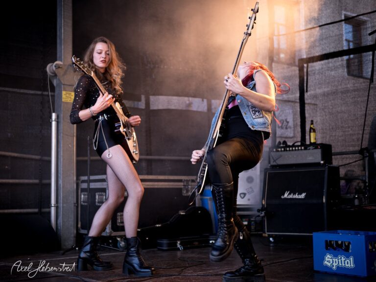 Zwei Rockmusikerinnen spielen leidenschaftlich auf einer Festivalbühne. – © Axel Hebenstreit