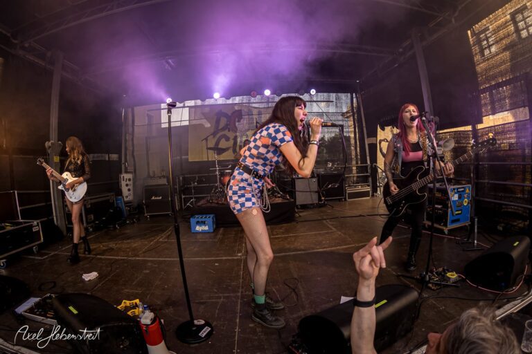 Drei rockende Musikerinnen mit energiegeladenem Auftritt auf einer Festivalbühne – © Axel Hebenstreit