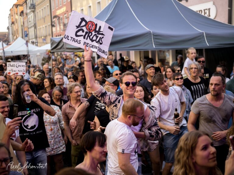 Menschenmenge auf einem Festival, einer jubelnden Person mit einem Schild über den "Doll Circus" in Regensburg – © Axel Hebenstreit