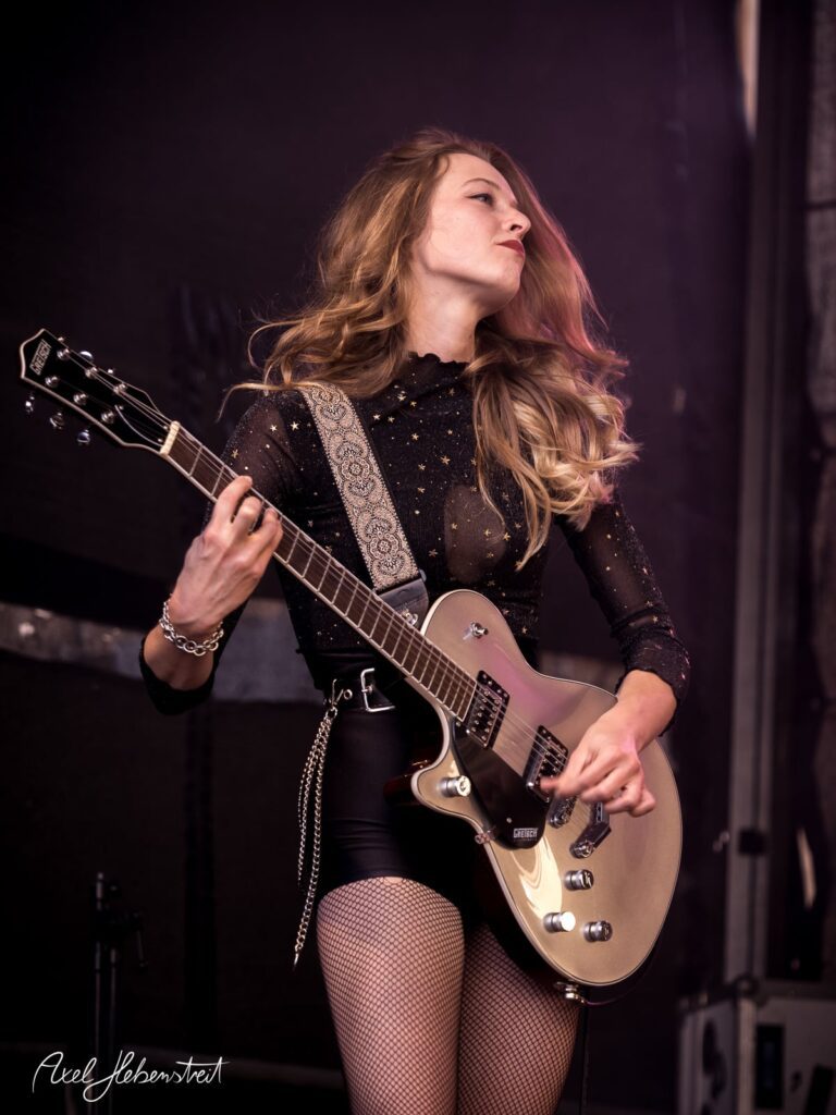 Eine Musikerin spielt leidenschaftlich Gitarre auf der Bühne und versprüht Energie und Leidenschaft. – © Axel Hebenstreit