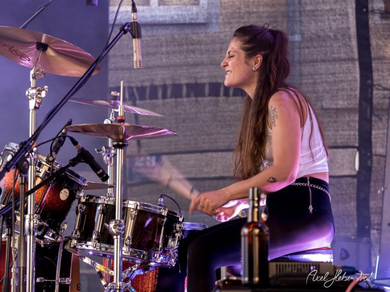 Drummerin spielt leidenschaftlich in einer energiegeladenen Live-Performance auf der Bühne – © Axel Hebenstreit