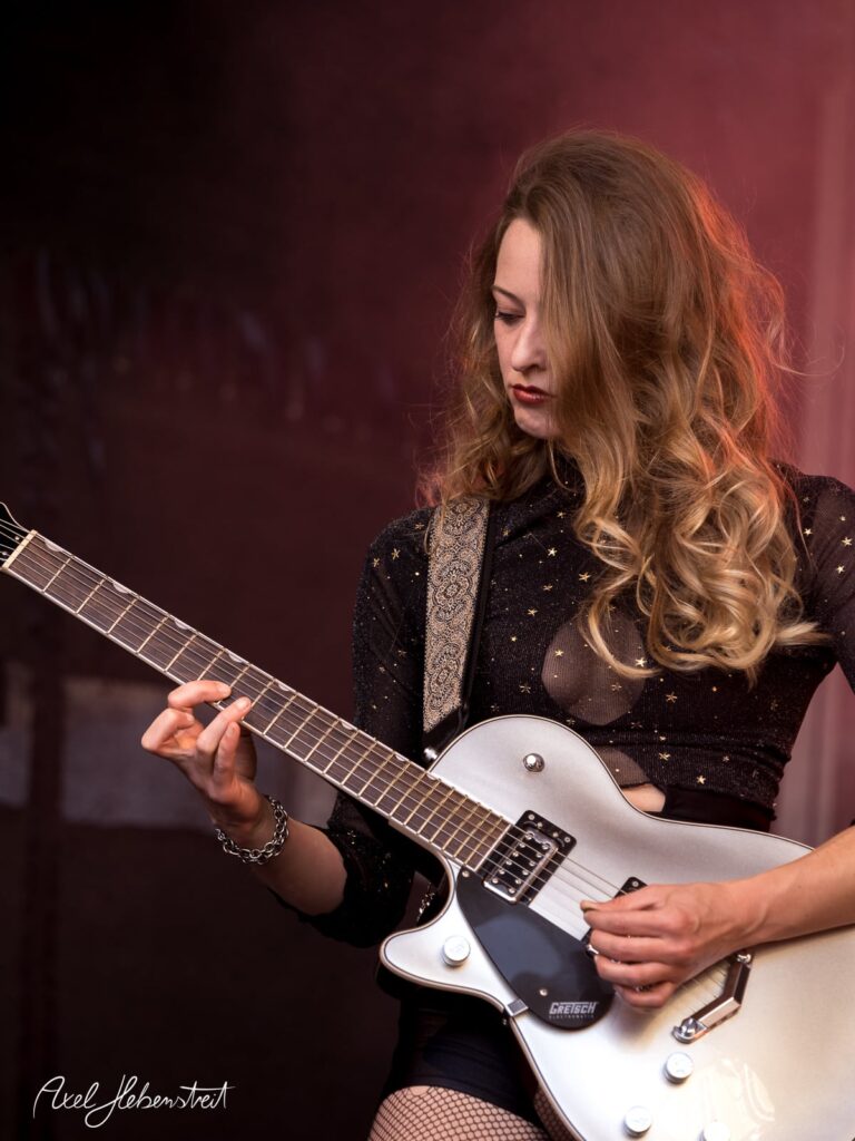 Eine Musikerin spielt leidenschaftlich Gitarre auf einer Bühne bei einem Festival. – © Axel Hebenstreit