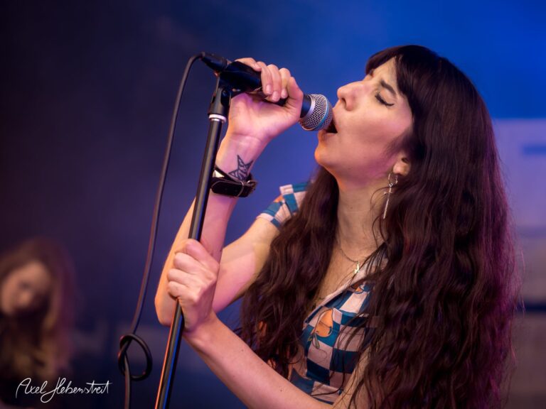 Singer in vintage outfit performs passionately on stage, capturing the energy of the concert – © Axel Hebenstreit.