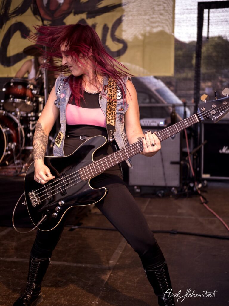Bassistin mit pinken Haaren spielt leidenschaftlich auf der Bühne eines Festivals – © Axel Hebenstreit