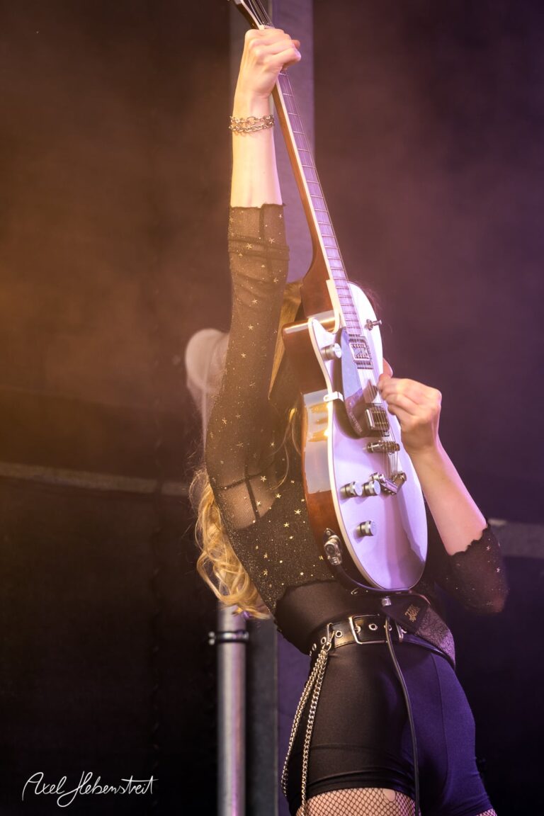 Fesselnde Musikerin mit E-Gitarre in spannungsgeladener Pose auf der Bühne – © Axel Hebenstreit