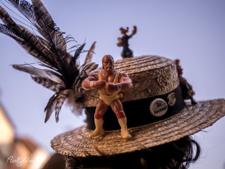 Ein bunter Strohhut mit Spielfiguren und Federn, der die kreative Stimmung eines Festivals einfängt – © Axel Hebenstreit