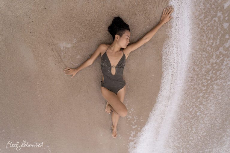 Eine Frau in einem Badeanzug liegt entspannt am Strand und genießt die sanften Wellen des Meeres – © Axel Hebenstreit