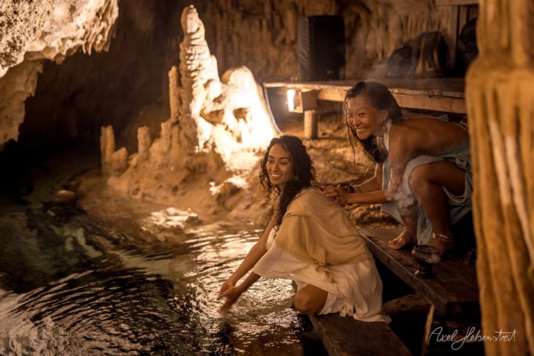 Zwei Frauen am Wasser in einer mystischen Höhle, die fröhlich miteinander interagieren – © Axel Hebenstreit