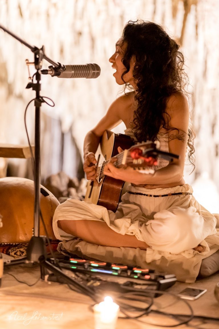 Musikerin spielt Gitarre in einer stimmungsvollen Höhle, umgeben von Kerzenlicht und natürlichen Felsformationen – © Axel Hebenstreit