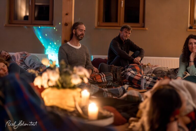 Eine meditative Gruppe von Menschen in einem warmen Raum, umgeben von Kerzenlicht und Decken, schafft eine ruhige Atmosphäre – © Axel Hebenstreit