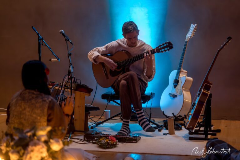 Ein Musiker spielt auf der Gitarre in einer stimmungsvolle Atmosphäre mit sanfter Beleuchtung – © Axel Hebenstreit.